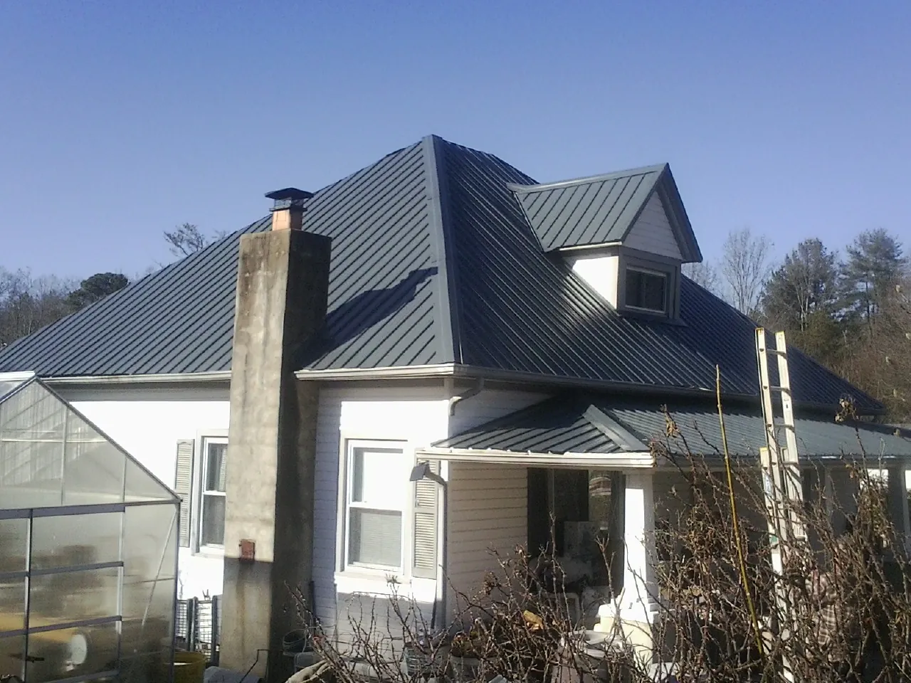 Dark blue standing seam metal roof on a white farmhouse with dormer — Slate & Tile Roof Repair by Roofing Brothers in Shannon