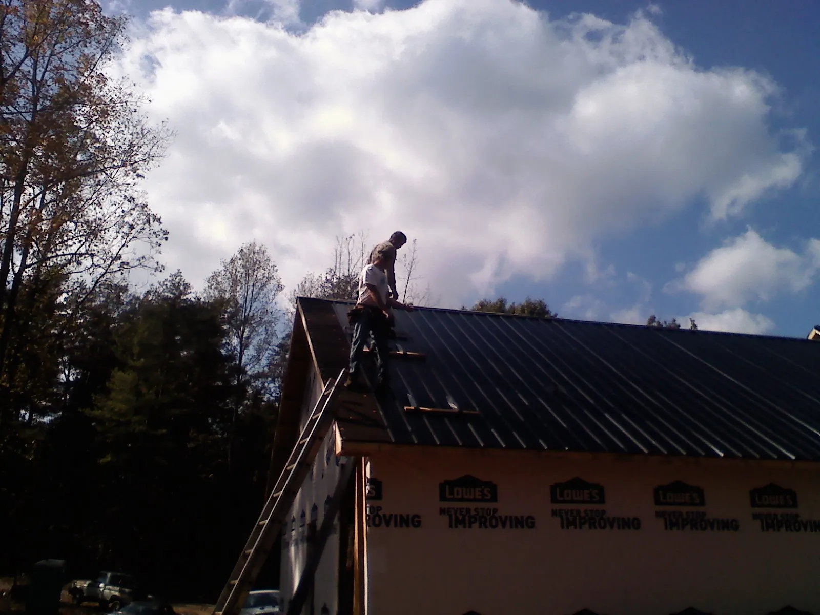 Roofer fastening dark metal panels high against a cloudy sky, from a Roof Inspection job in Shannon